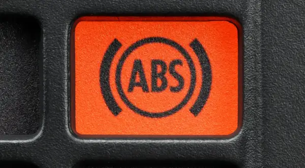 Pomarańczowy przycisk z symbolem ABS na desce rozdzielczej samochodu.