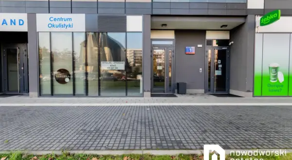 Elewacja budynku z witrynami sklepów: Centrum Okulistyki, Żabka. Widoczne szyldy i wejścia.