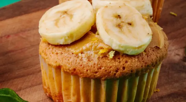 Pyszne muffinki bananowe fit z masłem orzechowym i plasterkami banana na drewnianej desce.