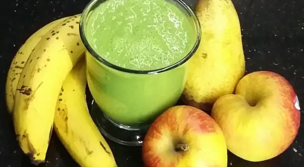 Zielony koktajl w szklance otoczony bananami, jabłkami i gruszką.