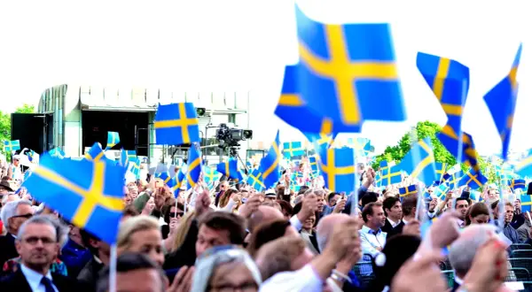 Stor folkmassa viftar med svenska flaggor. Många är lediga på nationaldagen och firar tillsammans.