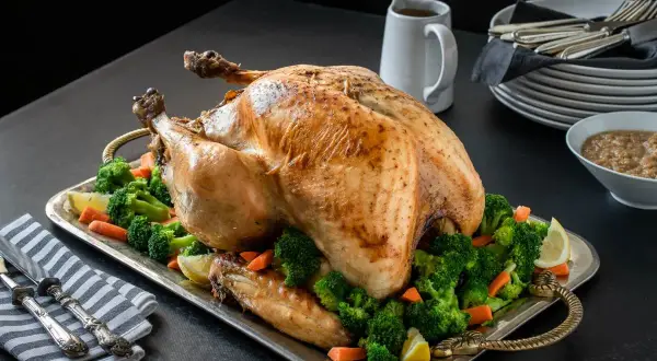 Un jugoso pavo relleno al horno, adornado con brócoli y zanahorias, listo para la celebración.