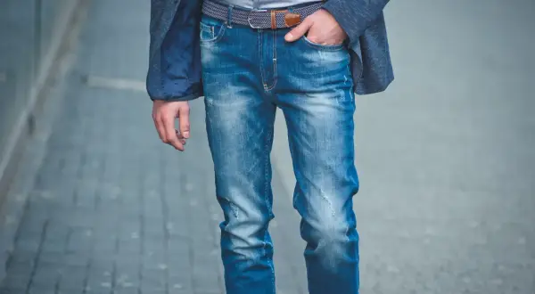 Mężczyzna w niebieskiej marynarce i modnych, przetartych jeansach. Różne rodzaje jeansów męskich można nosić na wiele sposobów.