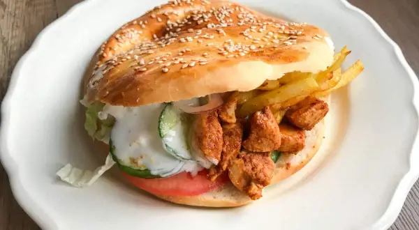 Kebab w bułce z kurczakiem, frytkami, warzywami i sosem na białym talerzu.