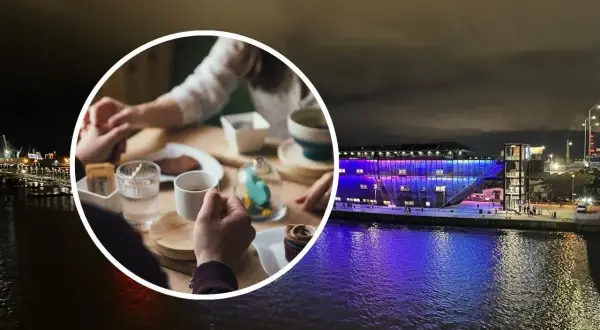 Para trzymająca się za ręce przy stoliku z kawą i ciastkiem, na tle nocnego Szczecina z oświetloną budowlą nad wodą.