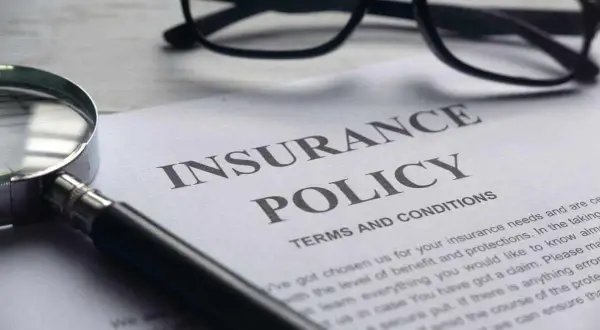 Okulary, lupa i dokument "Insurance Policy" symbolizują analizę polisy PZU po śmierci teścia.