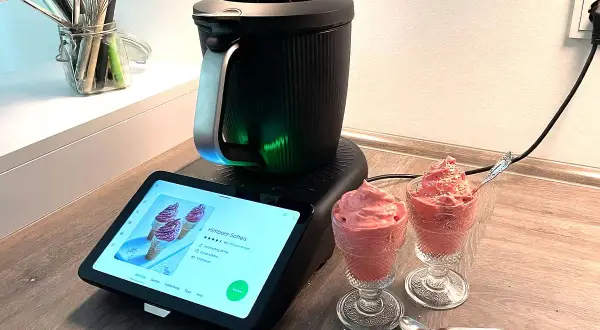 Moderne Eismaschine mit leckerem Heidelbeereis in Gläsern. Das Rezept wird auf dem Touchscreen angezeigt.