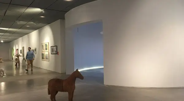 Un hombre pasea por una sala de exposiciones, admirando las obras de arte y una escultura de caballo. Una visita a los museos de Lugo.