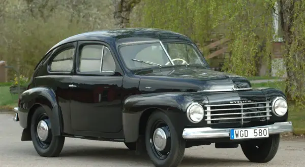 Svart Volvo PV 1954, en klassisk svensk bil, parkerad utomhus med grönska i bakgrunden.