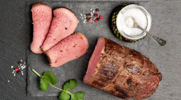 Una succulenta lombata di vitello, affettata e pronta per essere gustata, con sale grosso, pepe e un rametto di coriandolo.