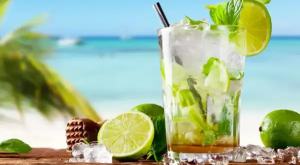 Szklanka orzeźwiającego mojito z limonką i miętą na tle plaży.