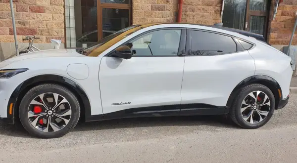Vit Ford Mustang Mach-E står parkerad utanför en tegelbyggnad. En cykel syns i bakgrunden. Detta är en ford mustang mach-e test.