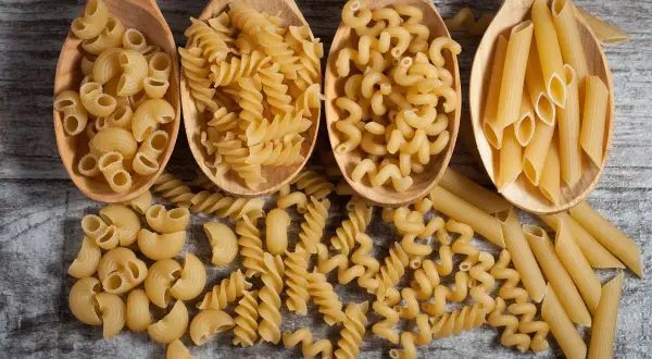 Vier Holzlöffel mit verschiedenen Nudelsorten: Maccheroni, Fusilli, Cavatappi und Penne. Eine Frage, wie viel Gramm Fusilli pro Person?