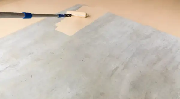 Application d'une peinture claire au rouleau sur un sol en béton, transformant l'espace pour peindre un parquet stratifié.