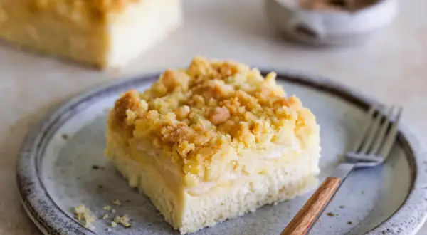 Ein Stück Blechkuchen mit Streuseln auf einem Teller, bereit zum Genießen. Dieses Rezept für Hefeteig Blechkuchen ist ein Klassiker.