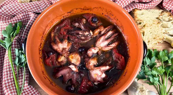Polipetti alla luciana in terracotta, con pomodoro, olive e pane tostato.
