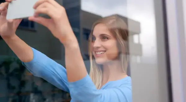 Uśmiechnięta blondynka robi sobie zdjęcie w lustrze, trzymając telefon.