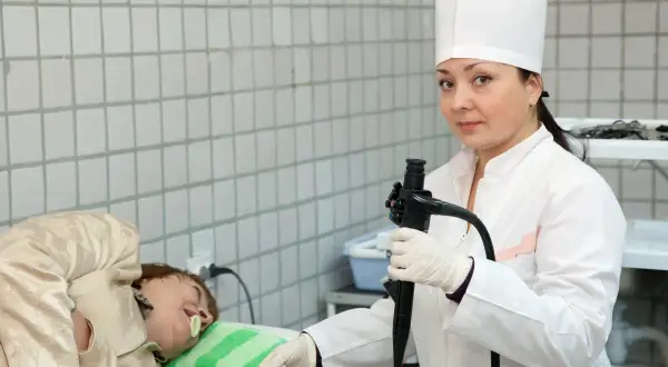 Lekarka w białym kitlu przygotowuje pacjenta do gastroskopii, trzymając endoskop.