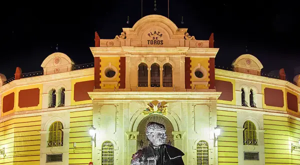 Estatua de un torero frente a la iluminada plaza de toros Almería por la noche.