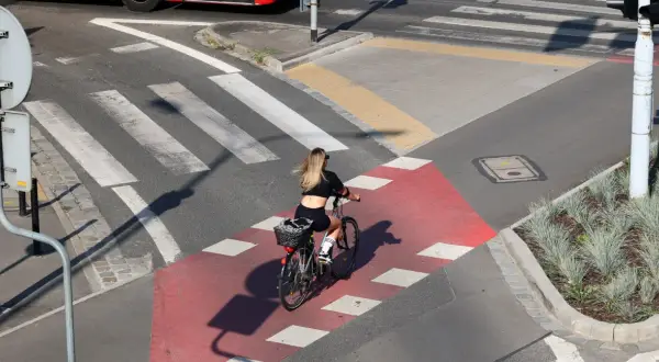 Kobieta na rowerze przejeżdża przez czerwony pas rowerowy, zbliżając się do **uwaga przejście dla pieszych**.