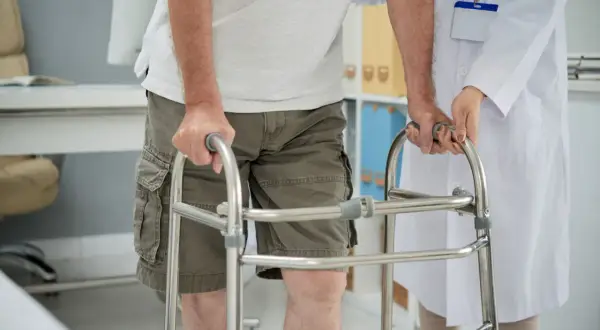Un uomo anziano, con una sensazione di camminare storto, si appoggia a un deambulatore mentre un medico lo assiste.