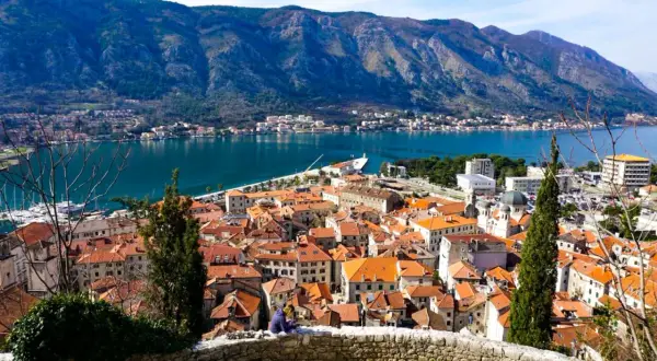 Widok na kotor stare miasto z czerwonymi dachami, zatokę i góry w tle.