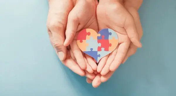 Dłonie trzymają serce z puzzli, symbolizujące wsparcie dla osób z autyzmem i ich unikalne wokalizacje.