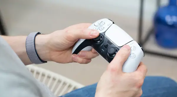 Hände halten einen weißen PS5-Controller, bereit für das PS4 auf PC streamen.