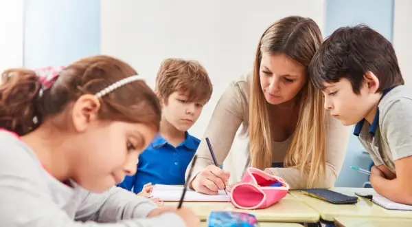 Lehrerin hilft Kindern in der Schule beim Schreiben.