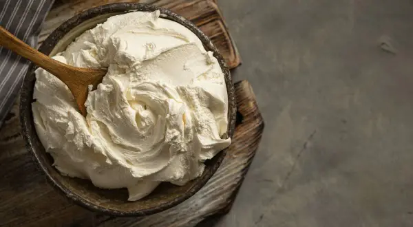 Kremowa masa w misce, idealna jako zamiennik mascarpone. Drewniana łyżka miesza gęsty, biały krem.