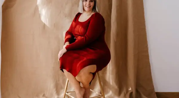 Uśmiechnięta kobieta w czerwonej sukience dresowej plus size siedzi na stołku.