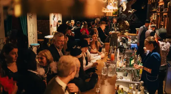 Goście w stylu retro bawią się w restauracji z muzyką na żywo w Warszawie. Przy barze panuje gwar, a atmosfera jest gorąca.