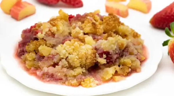 Ein Teller mit warmem Erdbeer-Crumble, garniert mit frischen Erdbeeren und Apfelstücken.