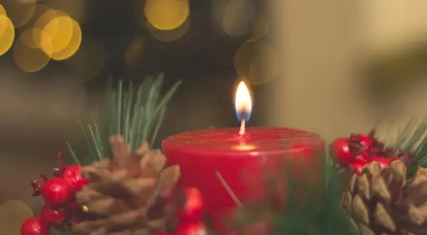 Ein Adventskranz mit brennender Kerze, Tannenzweigen, Zapfen und Beeren. Die Bedeutung des Adventskranzes liegt in der Vorfreude auf Weihnachten.
