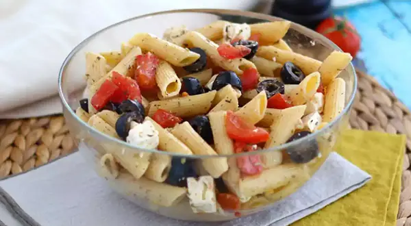 En härlig italiensk pastasallad med penne, tomater, svarta oliver och fetaost i en glasskål. Perfekt för en lätt lunch.