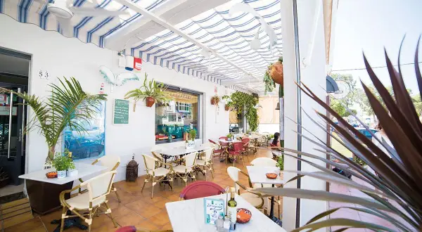Terraza de restaurante con mesas y sillas, toldos a rayas y vegetación. Un cartel anuncia "il brigantino san jose".