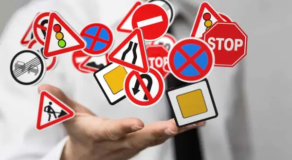 Main de personne tenant une multitude de panneaux de signalisation routière, dont certains indiquent la signification panneau interdiction poids lourds.