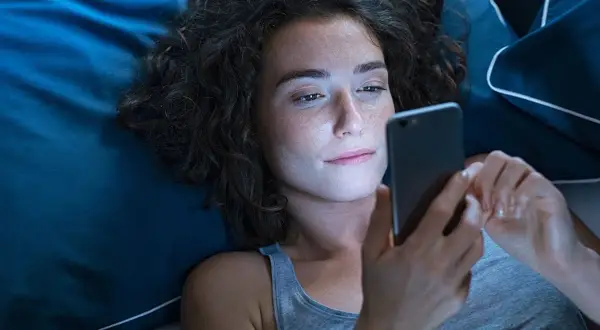 Dziewczyna leży w łóżku, przeglądając telefon. Może szuka wierszy na dobranoc dla dziewczyny, by wysłać je ukochanej.