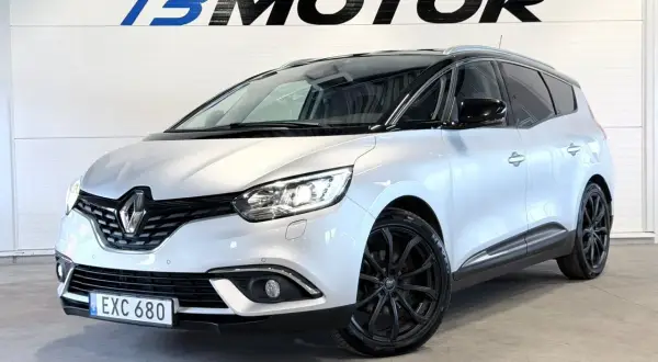 En silverfärgad Renault Grand Scénic med svarta fälgar står framför en vägg med logotypen B MOTOR.