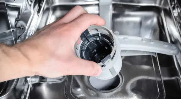 Ręka wyjmuje filtr zmywarki, który może być przyczyną, że zmywarka nie domywa.
