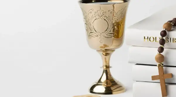 Złoty kielich, hostie, różaniec i stos białych ksiąg, w tym "Holy Bible". Symbolika sakramentu, jak akt chrztu.