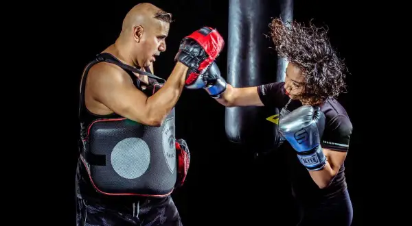 A boxer throws a powerful 1-2 combo, her hair flying as she connects with the pads held by her trainer.