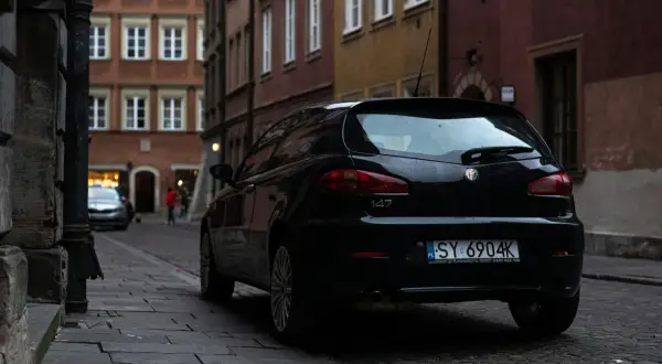 Czarny Alfa Romeo 147 na wąskiej uliczce. Czyj to numer rejestracyjny samochodu? SY 6904K.