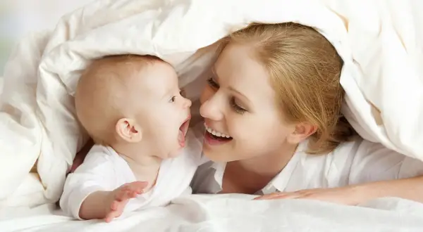 Mutter und ihr **baby 5 wochen** alt kuscheln unter einer Decke und lachen sich an.