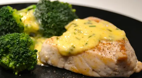 En saftig fiskfilé med krämig sås till tonfisk och gröna broccolibuketter på en svart tallrik.