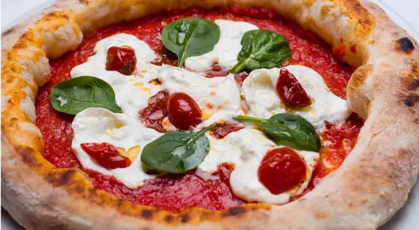 Deliciosa masa de pizza napolitana con tomate, mozzarella fresca, tomates cherry y hojas de albahaca.