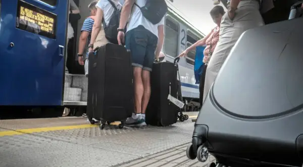Ludzie z dużymi walizkami na peronie PKP, wsiadający do pociągu.