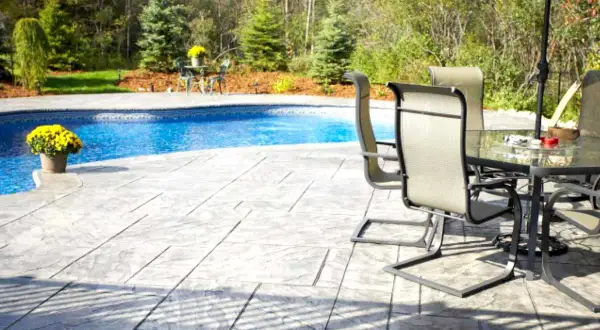 Un'area piscina con **cemento stampato carrabile** che imita la pietra, tavoli e sedie sotto un ombrellone.