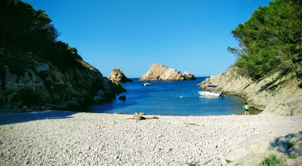 La cala Ferriol, con su playa de guijarros y aguas cristalinas, invita a disfrutar del sol y el mar. Barcas y bañistas comparten este paraíso.