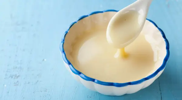 Cuchara con leche evaporada, un ingrediente cremoso y dulce, ideal para postres.